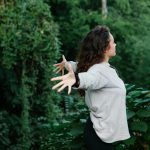 young woman spreading arms in freedom standing among greenery