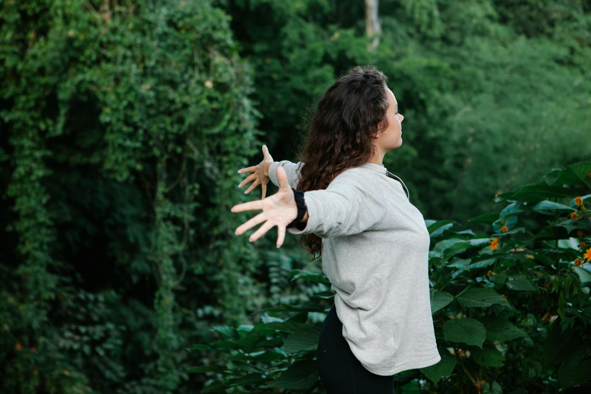 young woman spreading arms in freedom standing among greenery