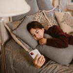 woman lying on bed while using cellphone