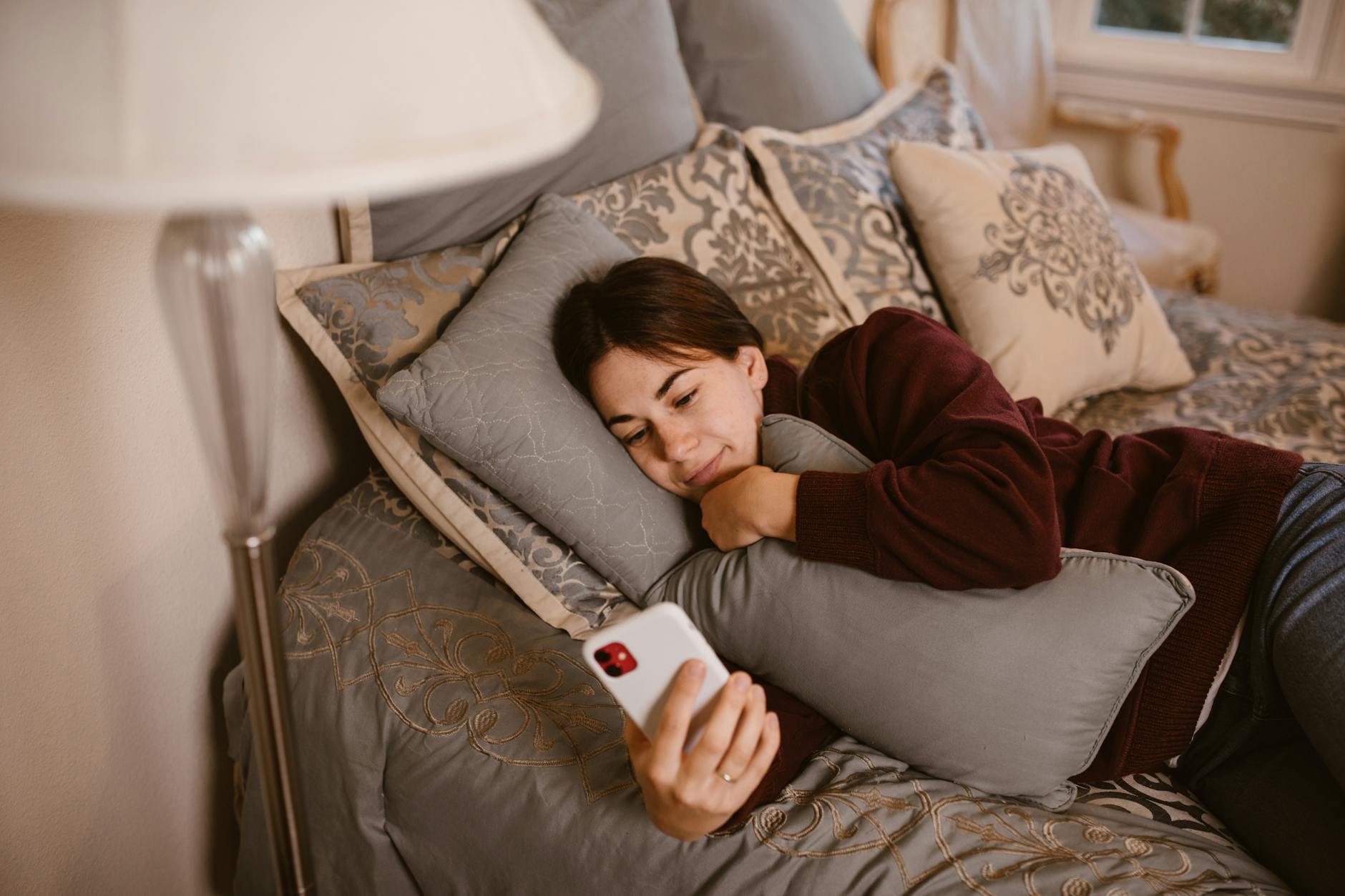 woman lying on bed while using cellphone