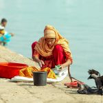 woman washing clothes on riverbank with crows