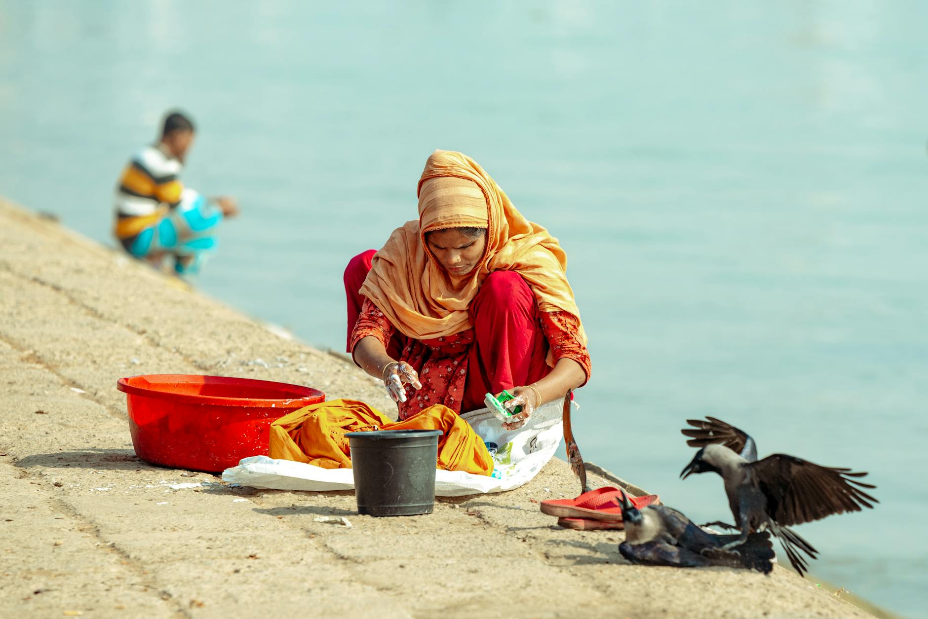 woman washing clothes on riverbank with crows