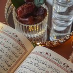 close up of open quran lying on a table next to dried dates and a glass of water