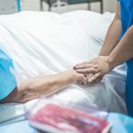 person in blue scrubs holding the hand of a patient lying on bed