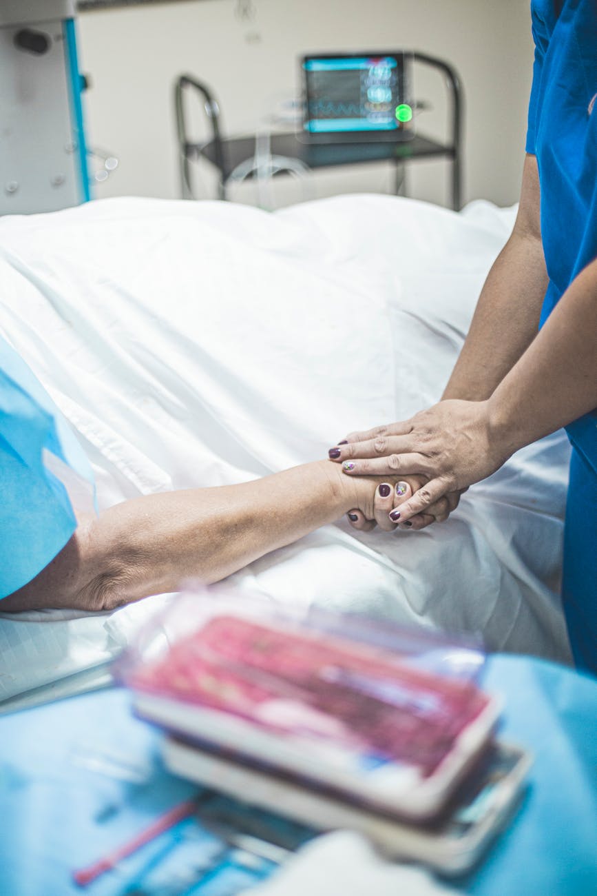 person in blue scrubs holding the hand of a patient lying on bed