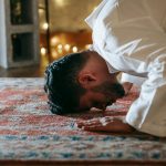 man in white thobe bowing down on red and blue rug