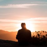 silhouette of person sitting and facing mountain during sunset