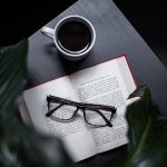 eyeglasses on opened book beside cup of coffee on table