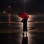 person holding red umbrella standing on wet road