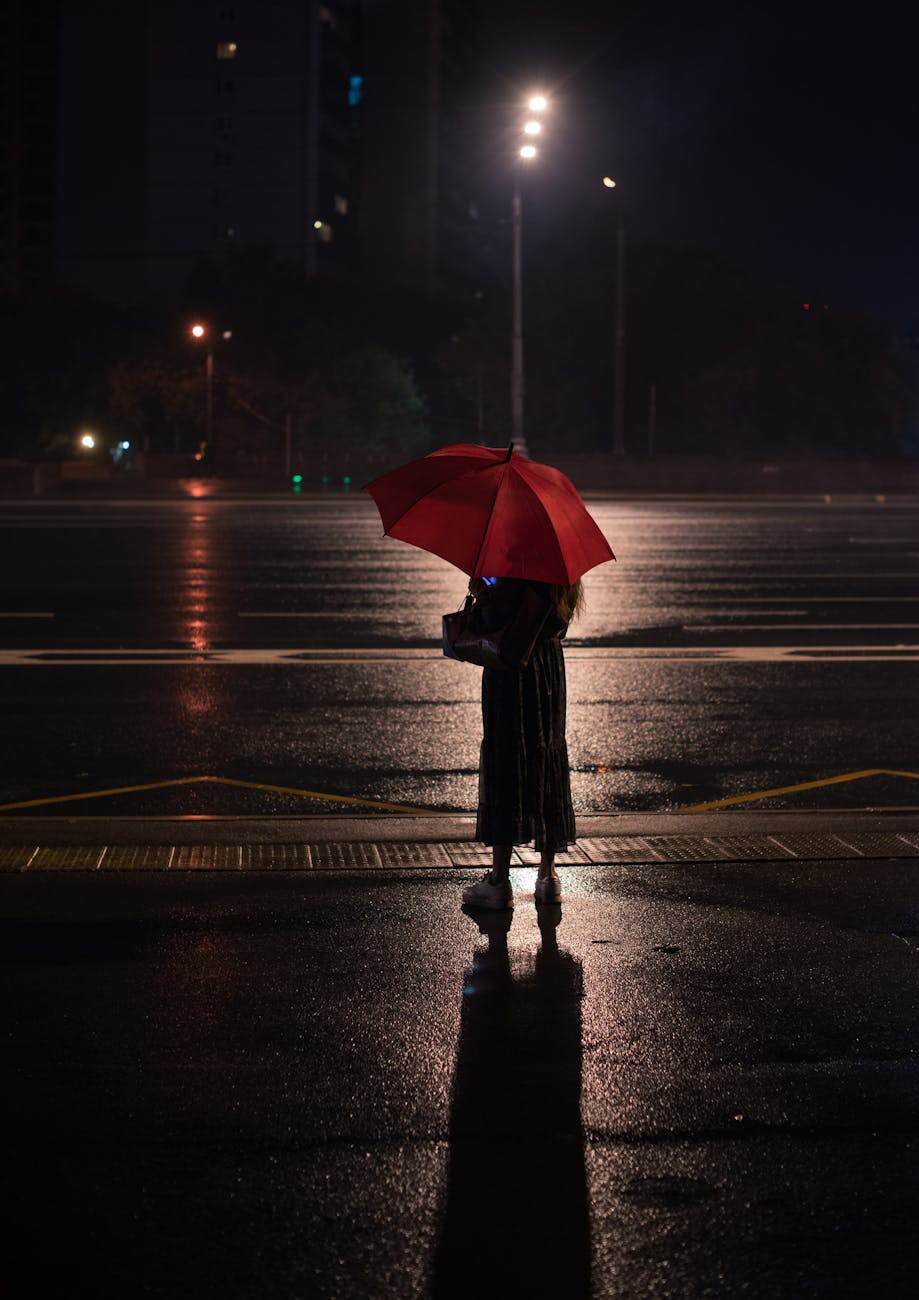 person holding red umbrella standing on wet road