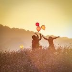 children playing with balloons on meadow at sunset