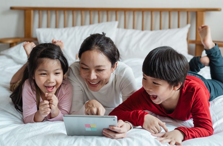 cheerful ethnic mother pointing at tablet screen and children watching and laughing
