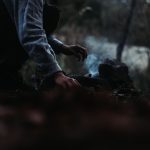 person crouching near smoke in darkness